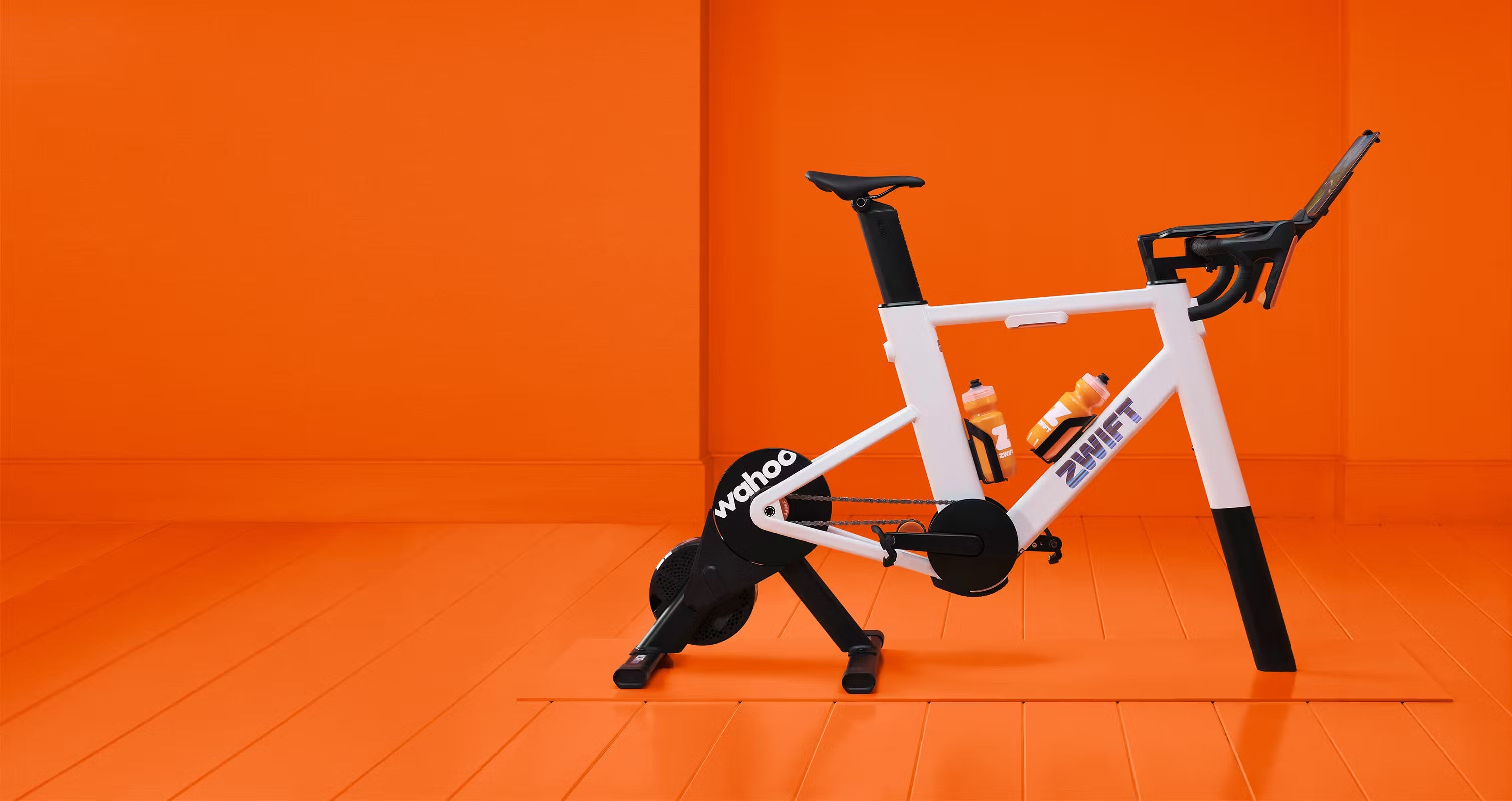 White exercise bike - Zwift Rid frame with Wahoo KICKR Core 2 trainer - with black accents on an orange background

